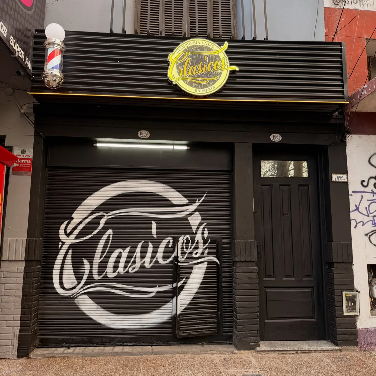 Frente de barbería Clásicos con persiana gráfica, cartel y poste de barbero
