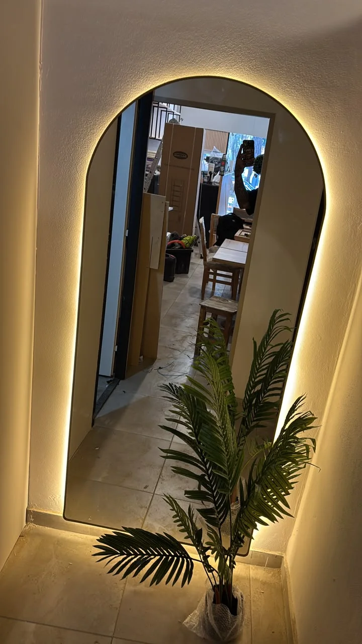 Espejo de arco con iluminación cálida y planta en cafetería