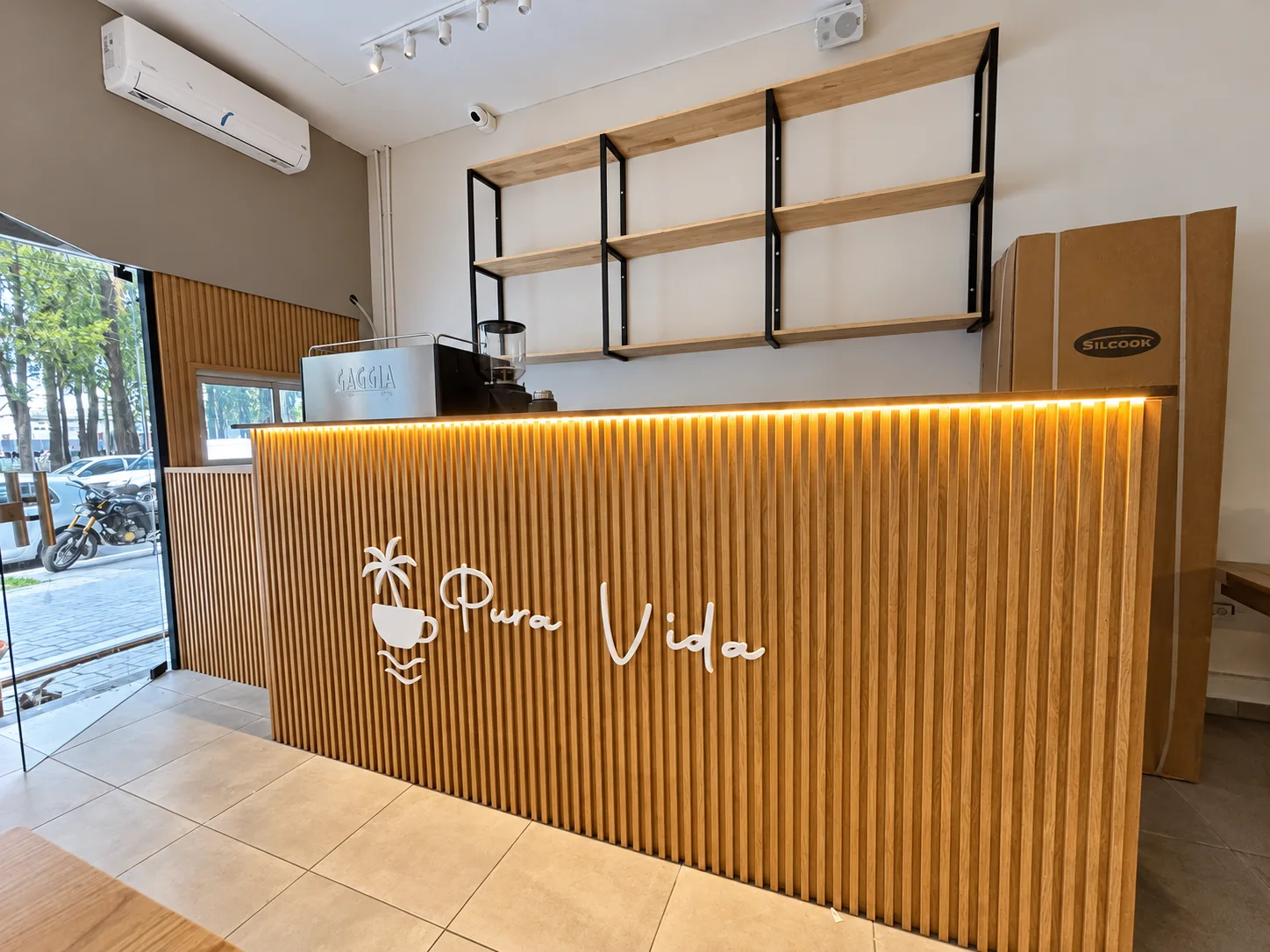 Mostrador con listones de madera, mesada oscura e iluminación cálida en cafetería Pura Vida