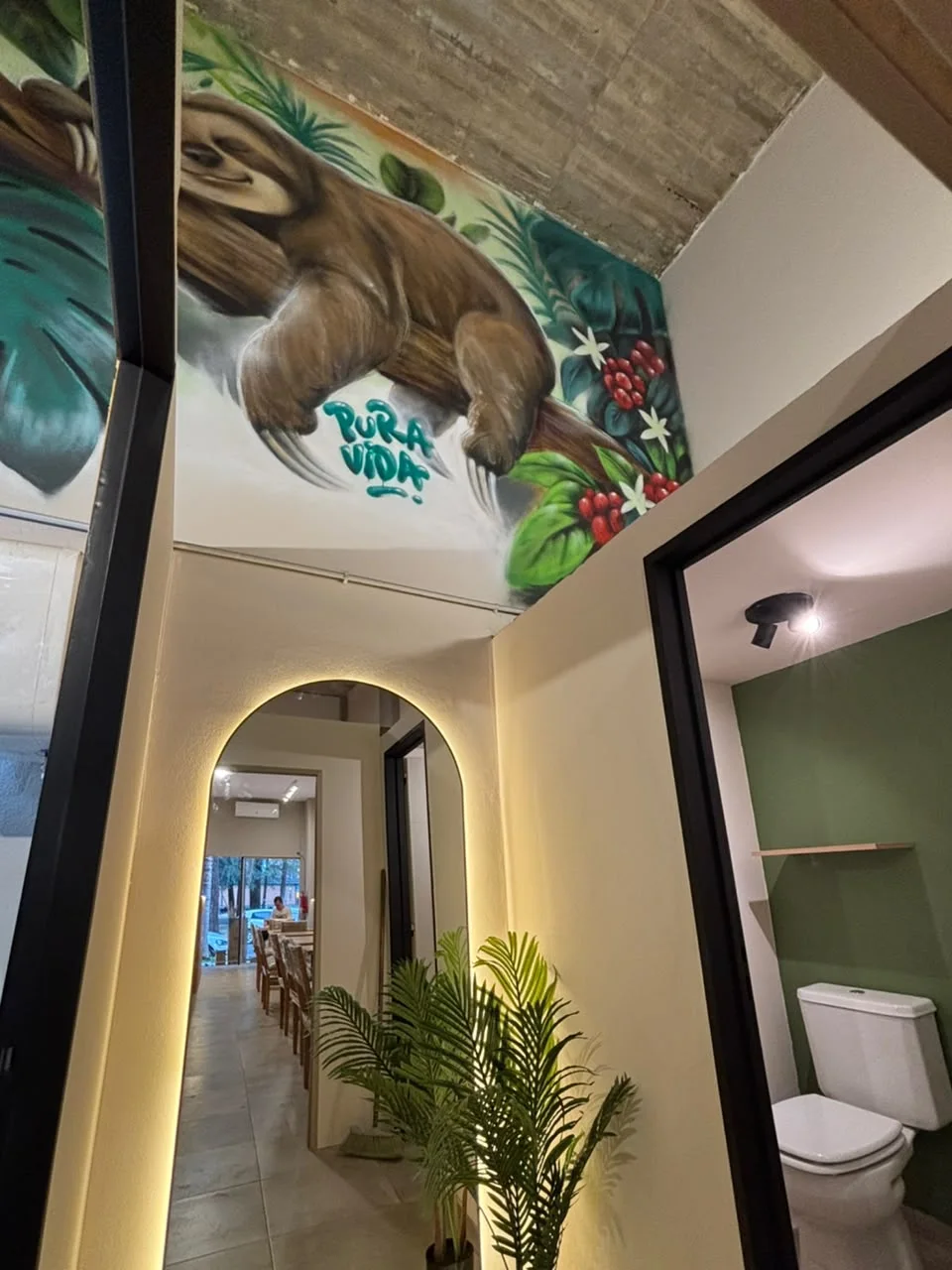 Mural de Pura Vida, plantas y espejo con iluminación en una cafetería